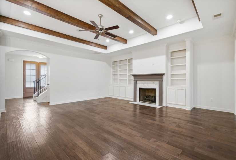 Living area featuring dark wood-finish flooring, a tray ceiling with exposed wood beams, and a ceiling fan