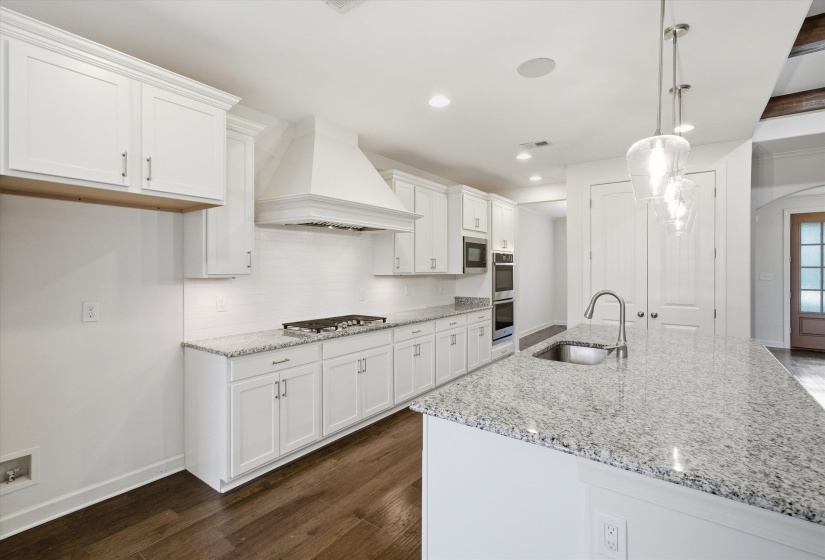 Bright kitchen featuring white shaker cabinetry, granite countertops, stainless steel appliances, a gas range with a custom range hood, and wood-finish flooring