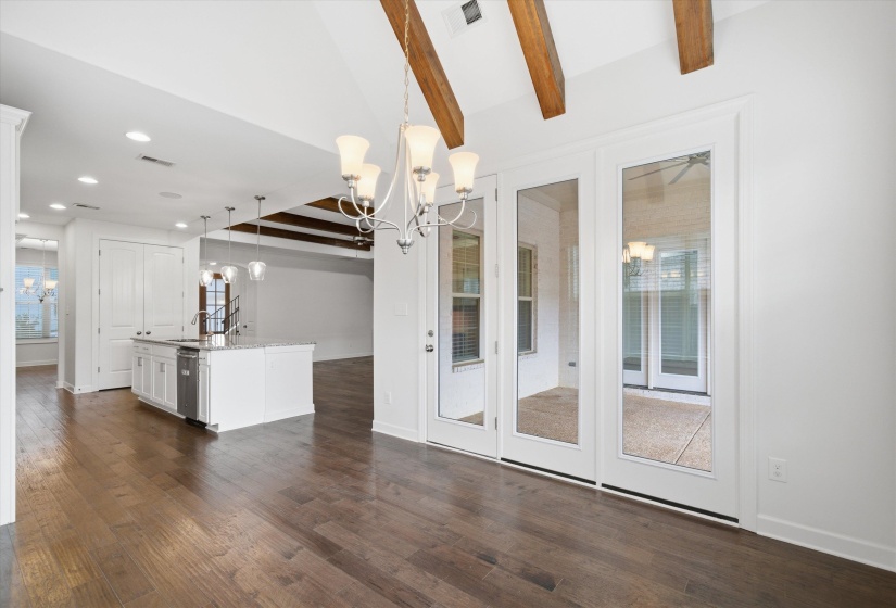 Spacious living area featuring wood-finish flooring, vaulted ceilings with exposed beams, and a modern chandelier