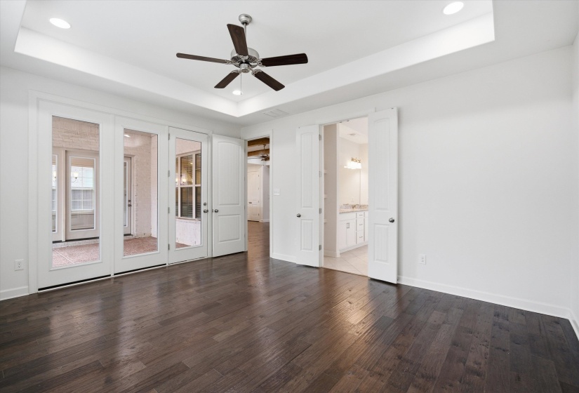 Spacious room featuring dark wood-finish flooring, a tray ceiling with recessed lighting, and a ceiling fan