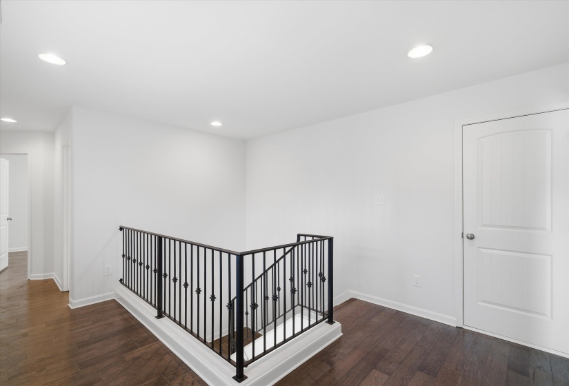 Upper landing featuring dark wood-finish flooring, white walls, and recessed lighting