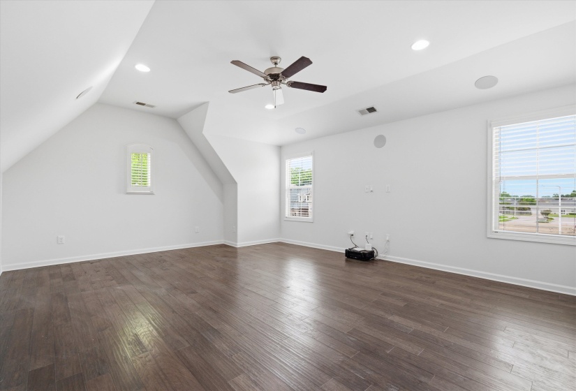 Spacious room featuring rich wood-finish flooring, multiple windows with blinds, a ceiling fan, recessed lighting, and integrated ceiling speakers