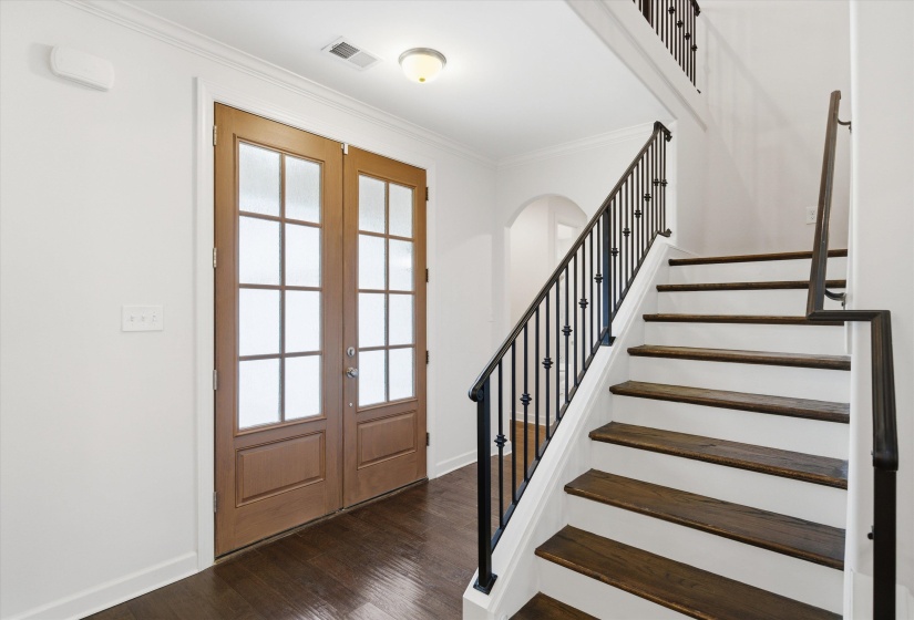 Entryway featuring wood-finish flooring, a grand staircase with dark wood treads and wrought iron balusters, and double panel-glass entry doors