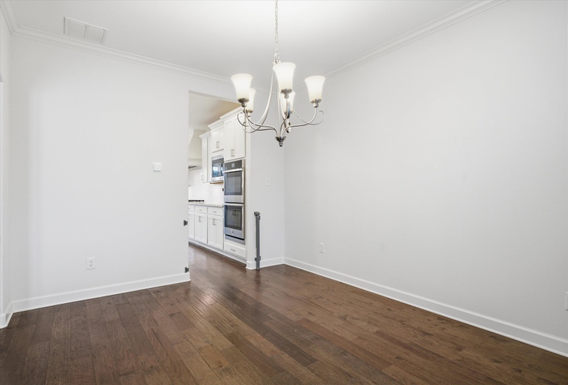 Spacious room featuring dark wood-finish flooring, white walls, and a contemporary chandelier