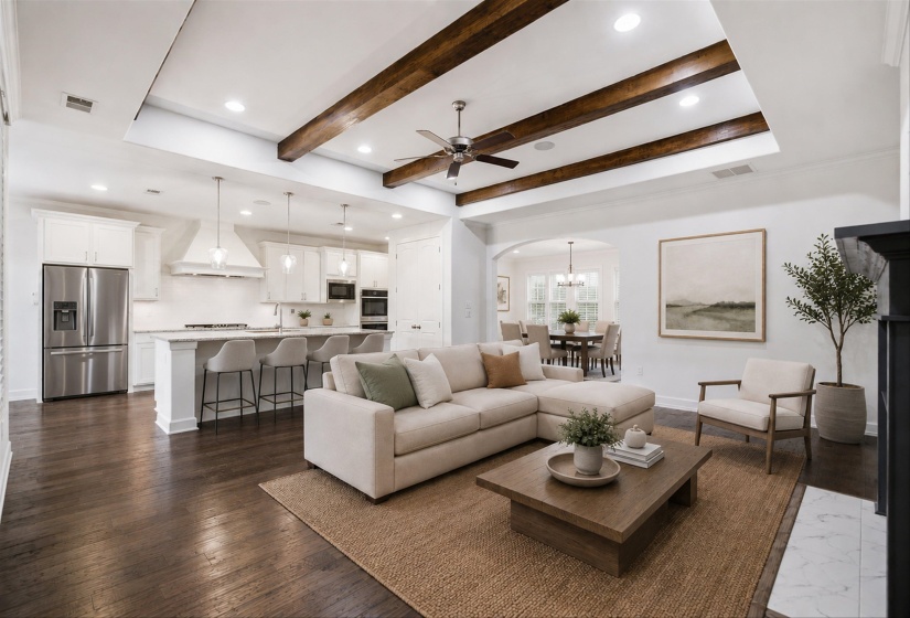 Expansive living area featuring coffered ceilings with exposed wood beams, dark wood-finish flooring, a contemporary fireplace with a white marble hearth, and an open-concept kitchen with stainless steel appliances and pendant lighting over a large island
