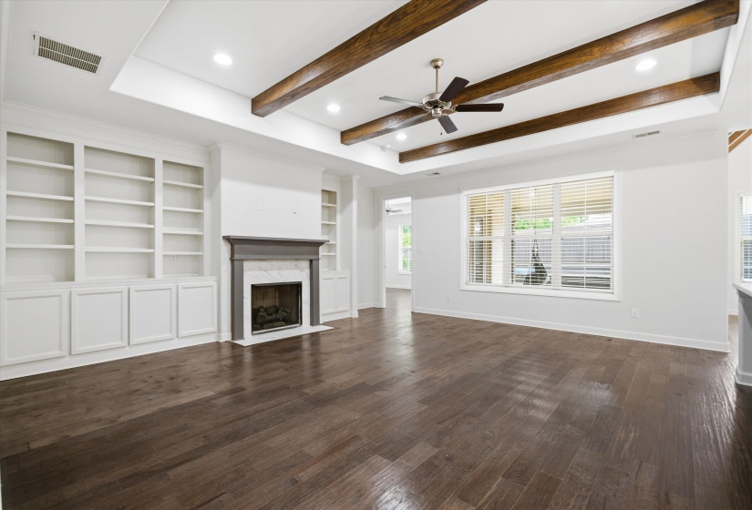 Spacious room featuring wood-finish flooring, a tray ceiling with exposed wood beams, and a ceiling fan