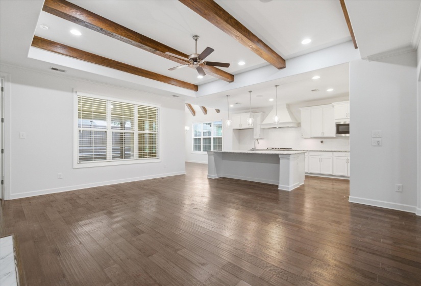 Expansive open-concept living space featuring wood-finish flooring and a kitchen with an island, white cabinetry, and pendant lighting