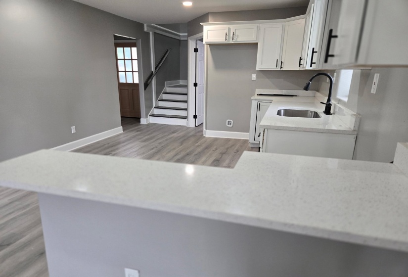 Modern kitchen featuring white cabinetry, light-toned countertops, a stainless steel sink with a matte black faucet, and a breakfast bar