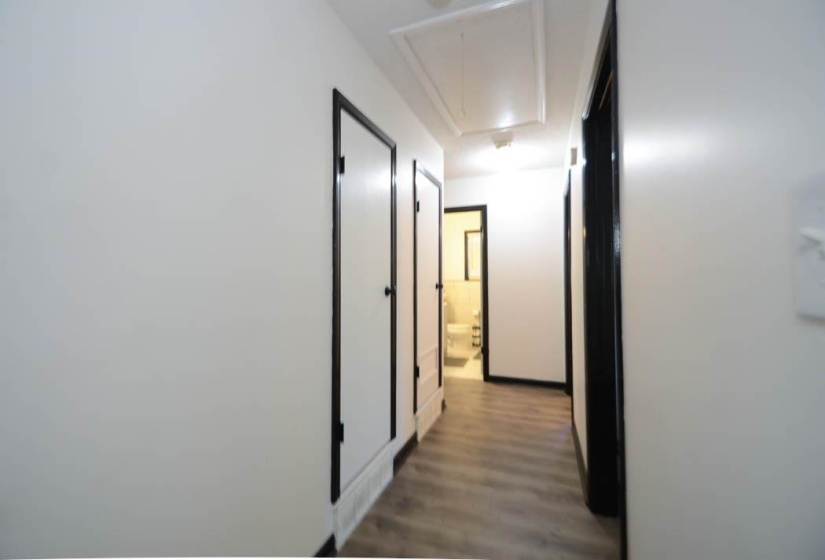 Hallway with wood-finish flooring, white walls, black trim, and multiple doors