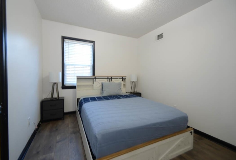 Bedroom featuring wood-finish flooring, white walls, and a window with blinds