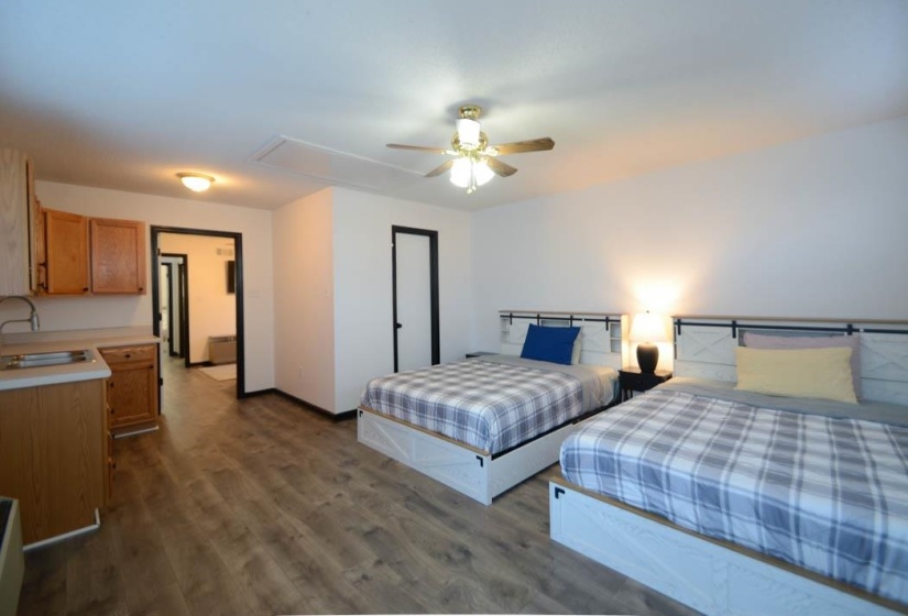 Open-concept space featuring wood-finish flooring, a ceiling fan with integrated lighting, and a kitchenette with wood cabinetry and a stainless steel sink