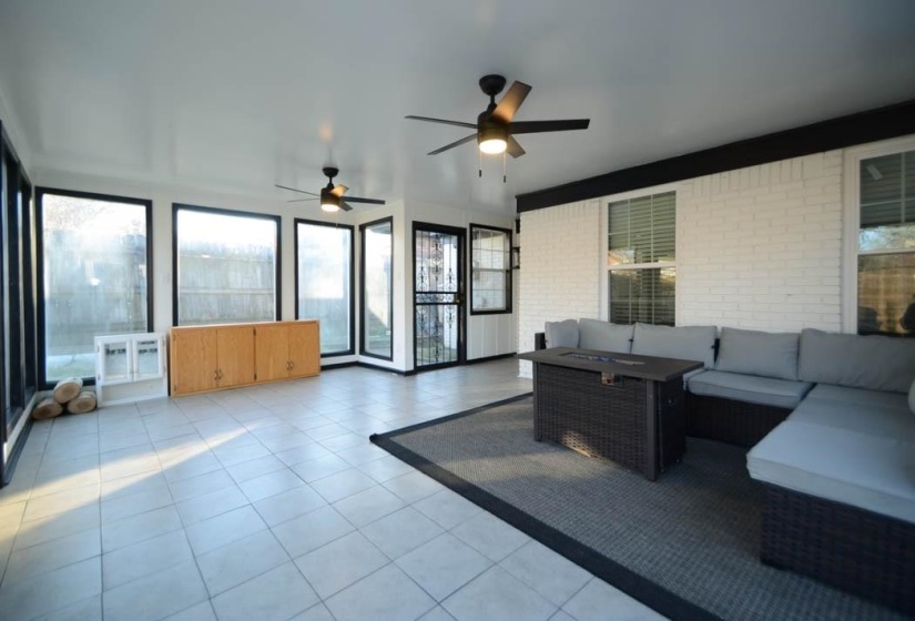 Enclosed patio featuring extensive window panels, tiled flooring, two ceiling fans, and a built-in wood cabinet
