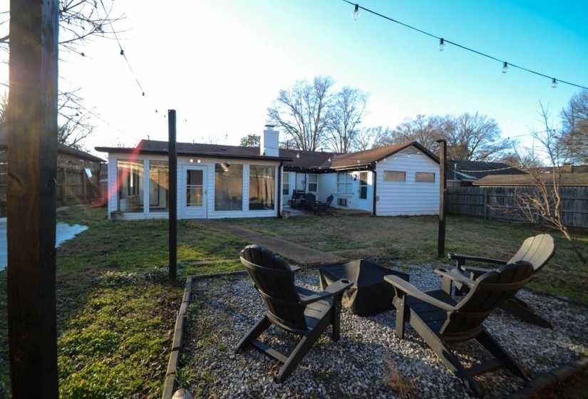 Expansive backyard featuring a gravel patio area with string lighting, a sunroom addition with large windows, and a white siding exterior