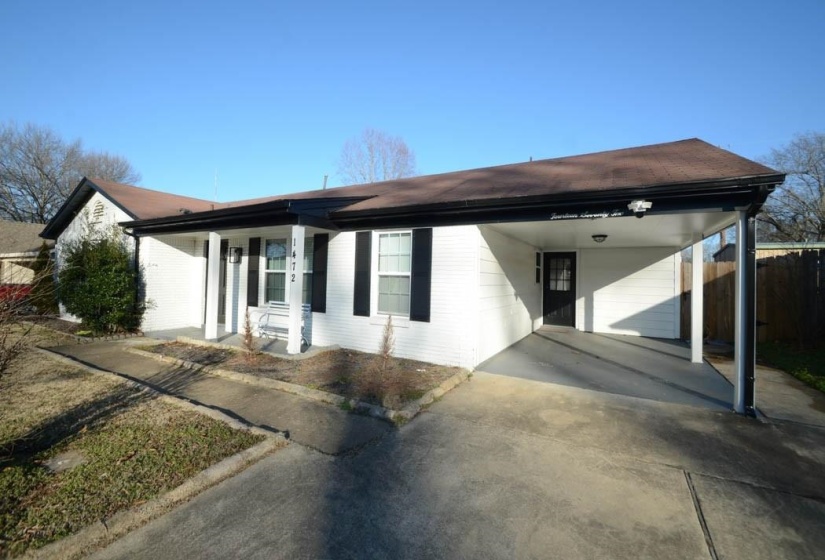White brick exterior with a brown shingle roof, featuring a covered carport, black window shutters, and a covered front entry with columns