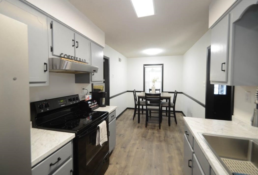 Galley kitchen featuring light gray cabinetry, laminate countertops, a black electric range, and wood-finish flooring