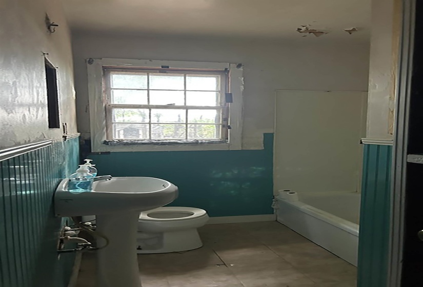 Bathroom featuring a window, pedestal sink, toilet, bathtub, and tile flooring