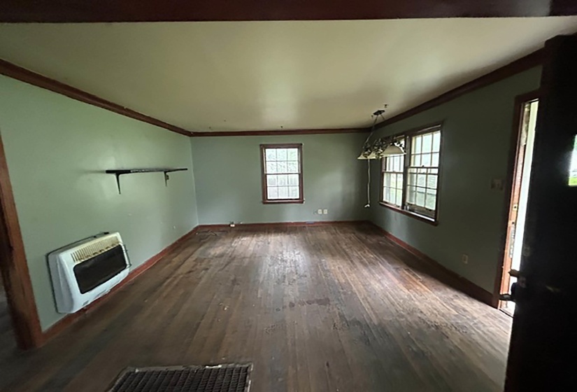 Spacious interior room featuring wood-finish flooring, two large windows, a ceiling-mounted light fixture, and dark wood trim