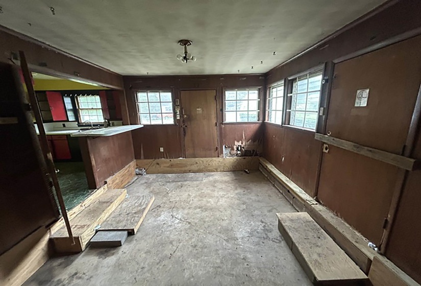 Open-concept room featuring multiple windows, a ceiling-mounted light fixture, and a pass-through counter to an adjacent room