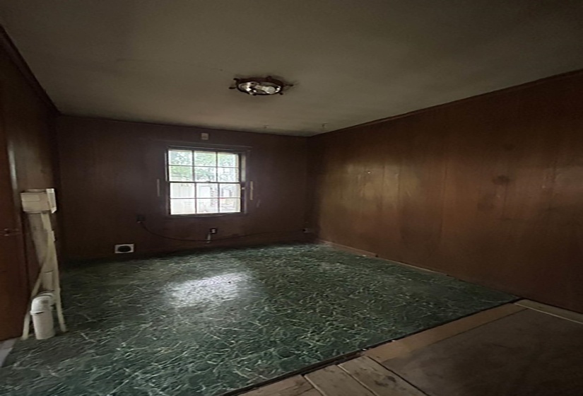 Room featuring wood paneling, a single window, and green patterned flooring