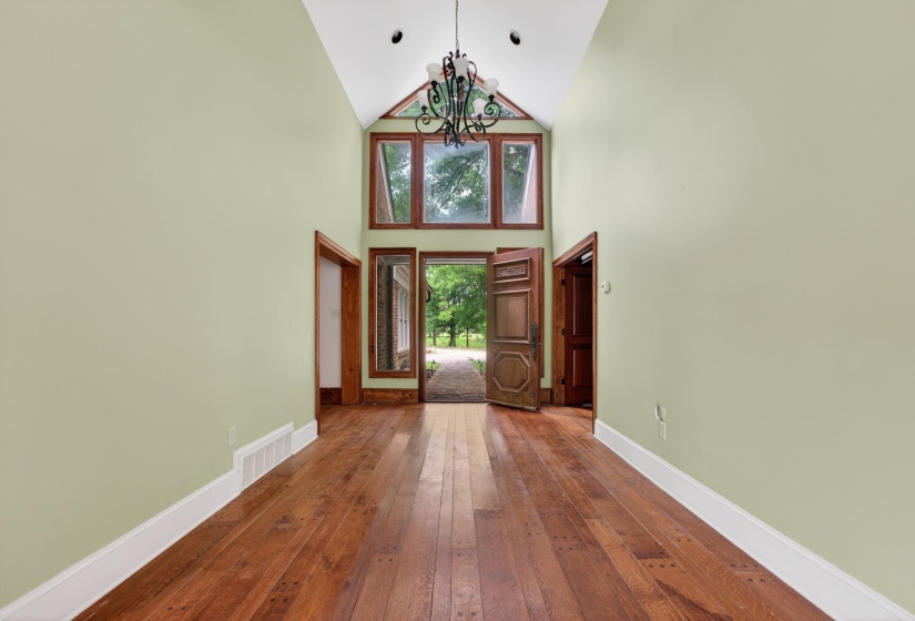 Vaulted entryway featuring wood-finish flooring, a decorative chandelier, and a wood-framed window wall