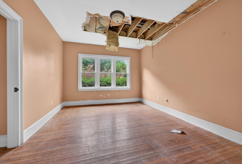 Room featuring wood-finish flooring, a multi-pane window with white trim, and a partially exposed ceiling