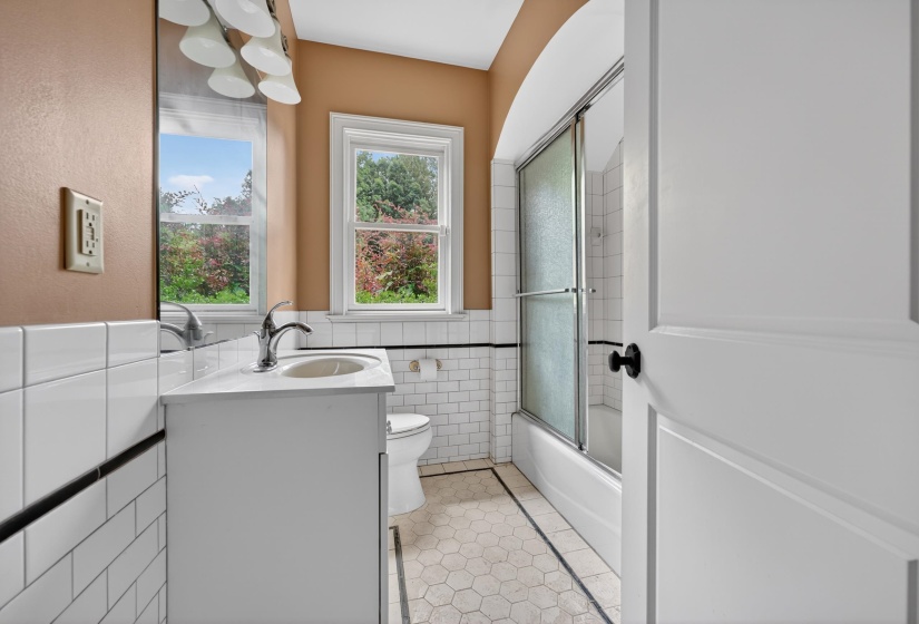 Bathroom featuring a single vanity with chrome faucet, white subway tile surround, hexagonal floor tile, and a tub with sliding glass doors