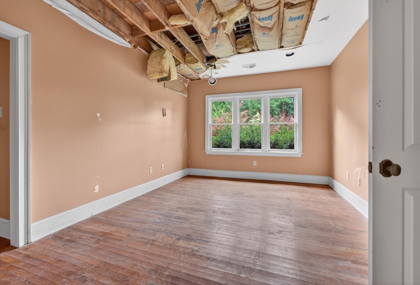 Room featuring wood flooring, three-panel window, baseboard molding, and an exposed ceiling structure with insulation