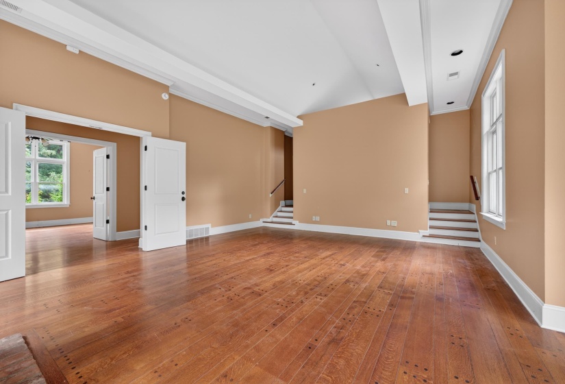 Spacious interior featuring wood-finish flooring, two sets of double doors, a large framed window, and a staircase with a wood handrail