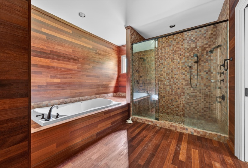Bathroom featuring wood-finish wall paneling, a built-in soaking tub with dark-finish fixtures, and a glass-enclosed shower with mosaic tile surround