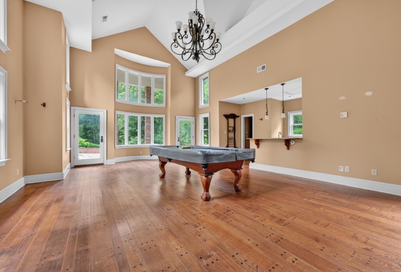 Expansive room featuring rich wood-finish flooring, soaring vaulted ceilings, and a decorative chandelier