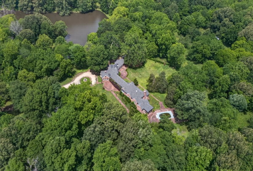 Expansive estate featuring a large residential structure, a circular driveway, an in-ground pool, a private pond, and extensive surrounding woodland