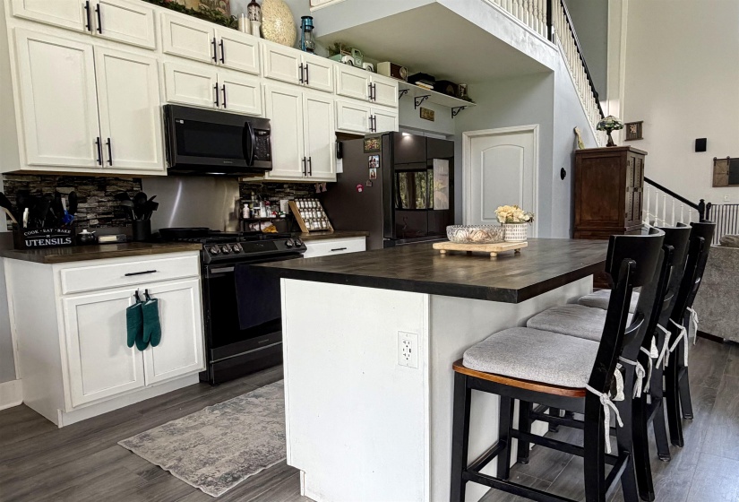 Open-concept kitchen featuring white shaker-style cabinetry, dark countertops, and a stone-tile backsplash