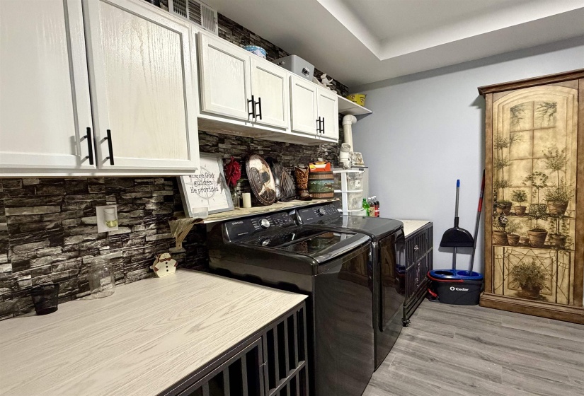 Laundry area featuring a stone-look backsplash, white upper cabinetry with black hardware, wood-finish countertops, and wood-finish flooring