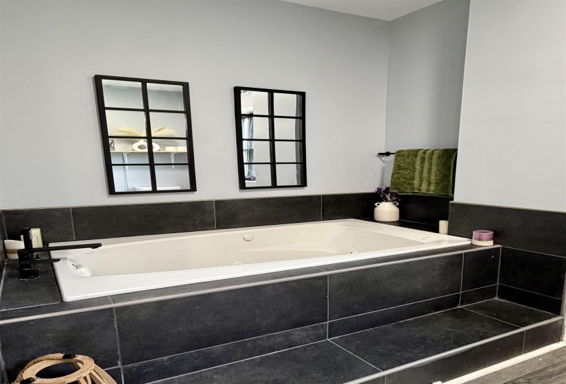 Soaking tub featuring a black tile surround and integrated steps