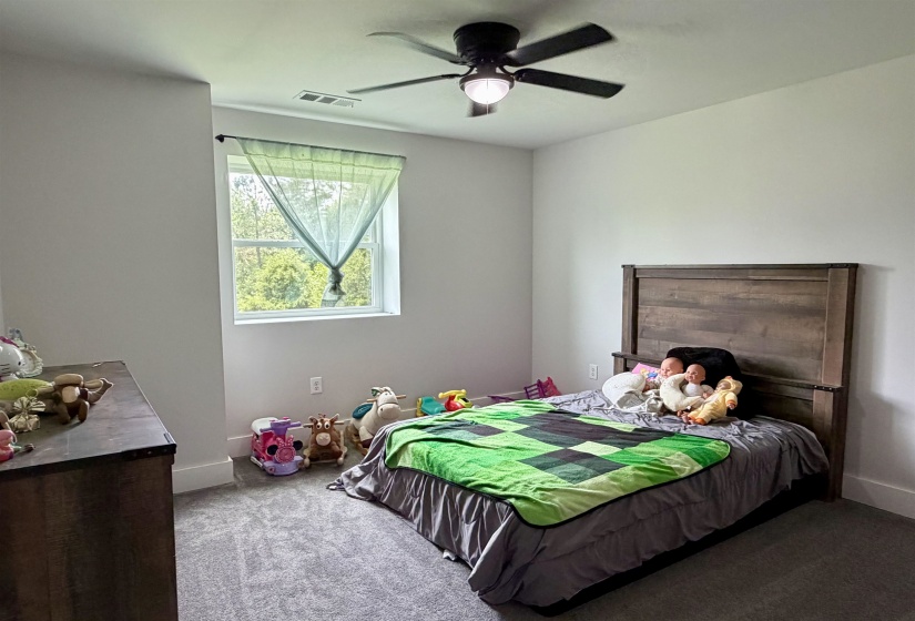Bright room featuring a window with exterior tree line, ceiling fan with integrated lighting, gray walls, and carpet flooring