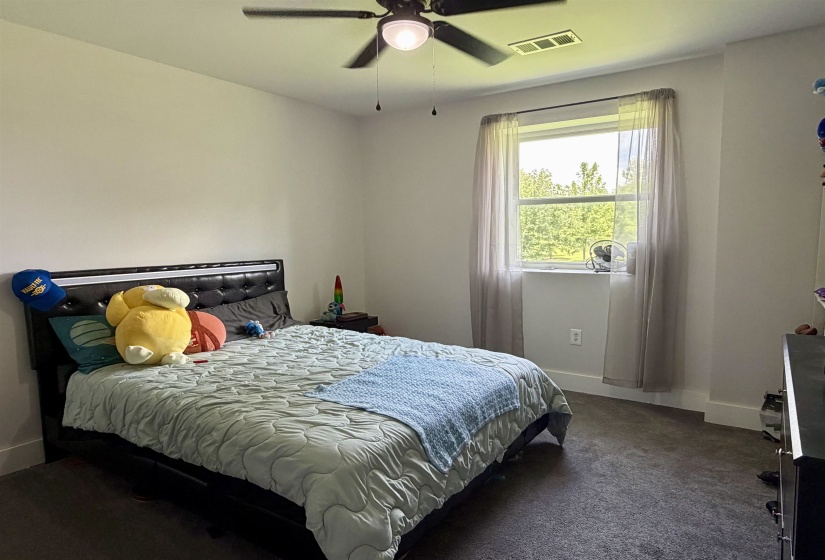 Bedroom featuring a window with sheer curtains, a ceiling fan with integrated lighting, and dark carpet flooring