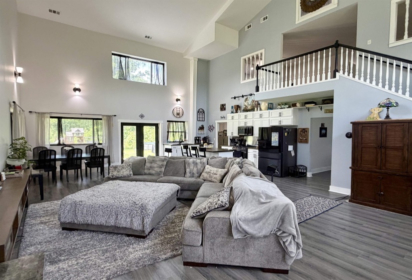 Spacious living area featuring high vaulted ceilings, wood-finish flooring, and a second-story balcony with white balusters and a dark handrail