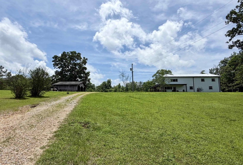 Gravel driveway leading to a white metal-sided residence with multiple windows and a covered porch