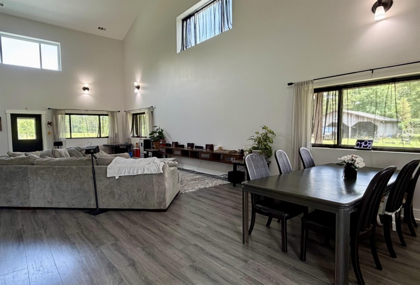Open-concept living space featuring vaulted ceilings, wood-finish flooring, ample natural light from multiple windows, and recessed wall sconces