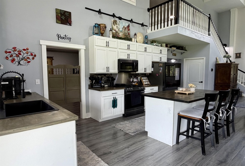 Kitchen with white cabinetry, black appliances, a central island with seating, wood-finish flooring, and a visible pantry entrance