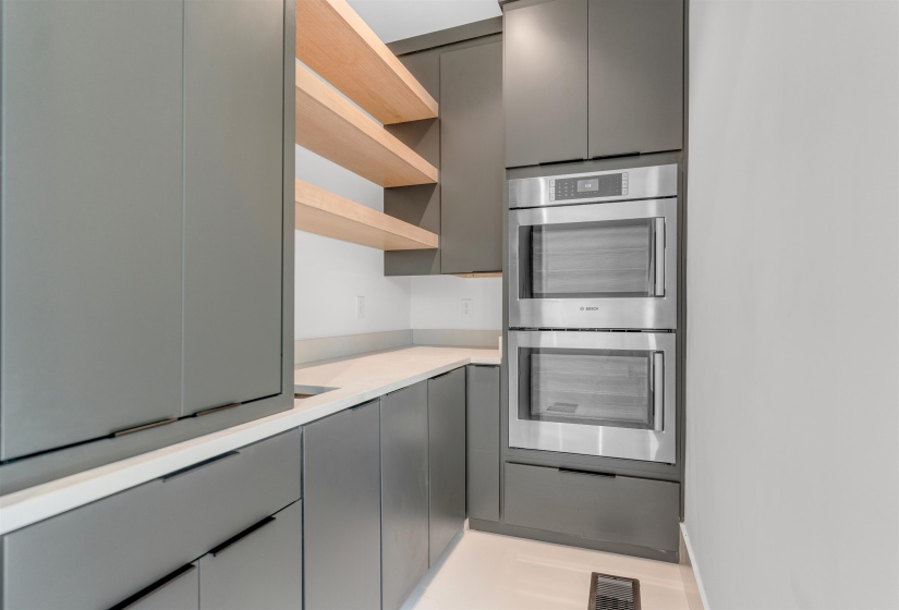 Kitchen with stainless steel double oven, open shelves, gray cabinetry, and light countertops