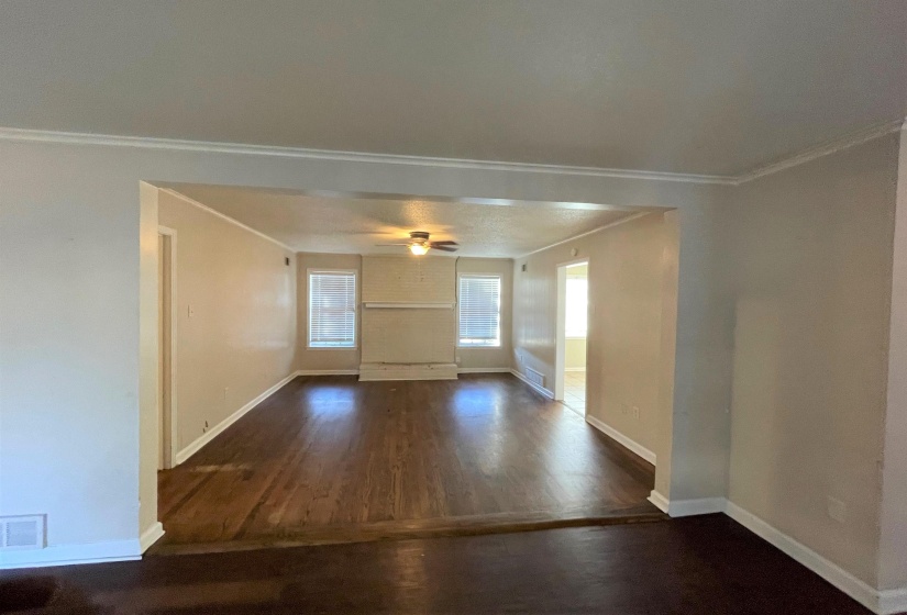 Spacious living area featuring wood-finish flooring, light neutral walls, white baseboards, crown molding, and a ceiling fan with integrated lighting