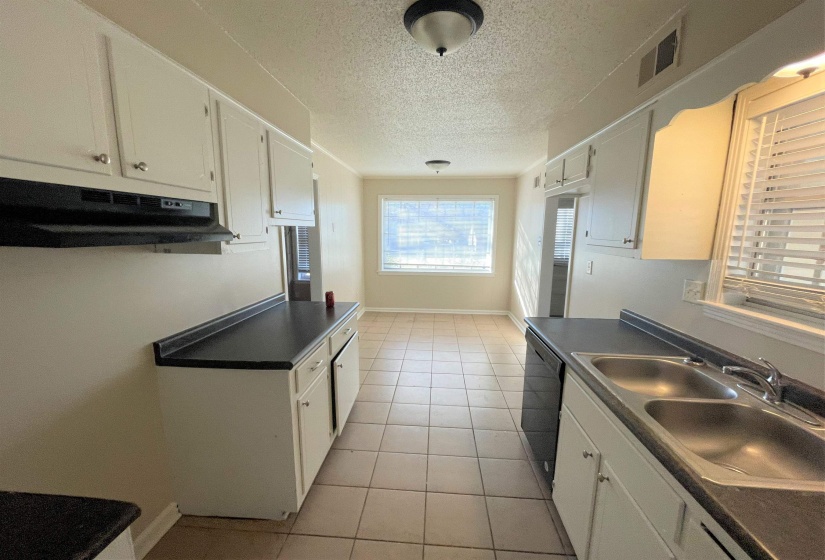 Functional kitchen featuring white cabinetry, dark countertops, a double basin sink, and tile flooring