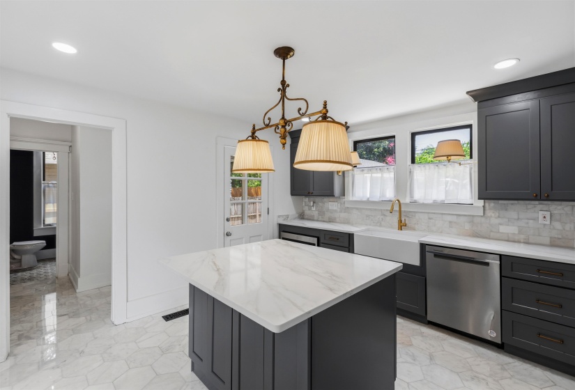 Kitchen featuring a central island with a white veined countertop, dark cabinetry, and white hexagonal floor tiling