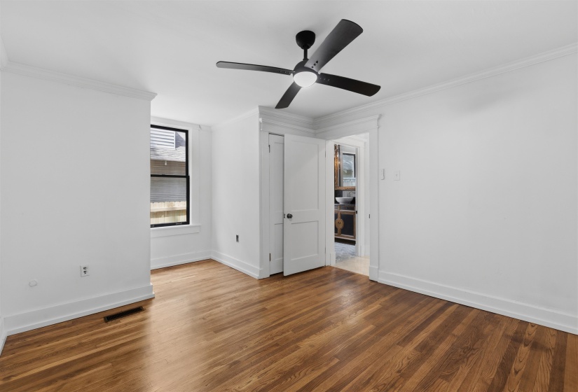 Room featuring wood-finish flooring, a contemporary ceiling fan with integrated lighting, white walls, and elegant crown molding