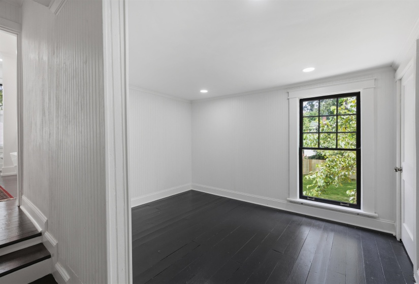 Room featuring dark wood-finish flooring, white beadboard walls, and a black-framed window with exterior greenery