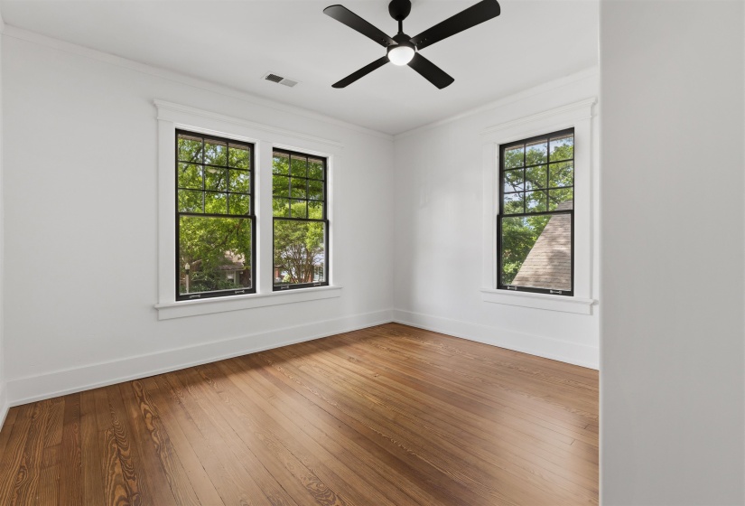 Spacious room featuring rich wood-finish flooring, white walls, and a contemporary black ceiling fan with integrated lighting