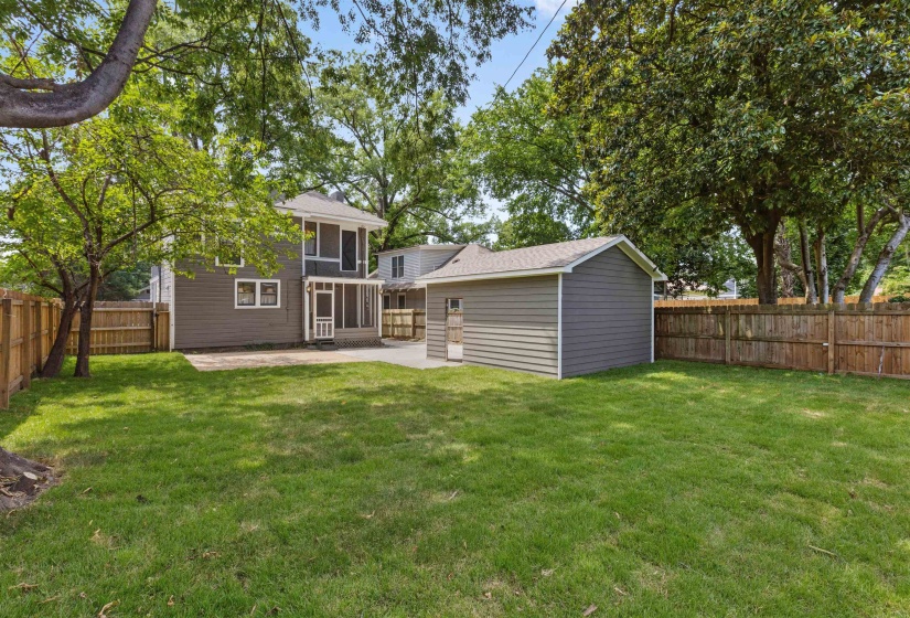 Expansive backyard featuring a manicured lawn, established trees, and a privacy fence