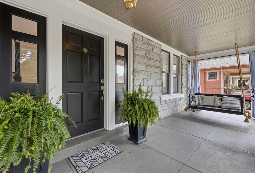 Covered front porch featuring a paneled entry door with sidelights, stone facade, and concrete flooring