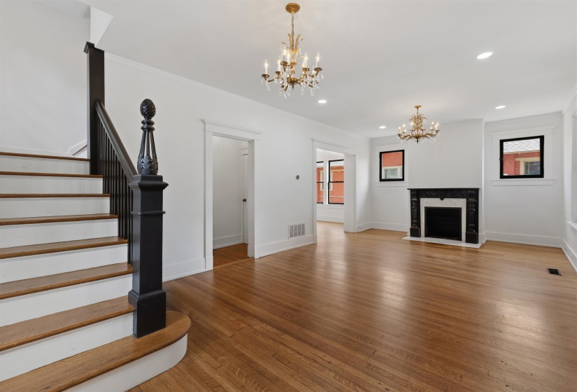 Spacious interior featuring wood-finish flooring, a decorative fireplace with a dark mantel, and two ornate chandeliers